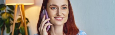 Modern oturma odasında gülümseyen ve akıllı telefondan konuşan mutlu stil sahibi kadın, yatay afiş.