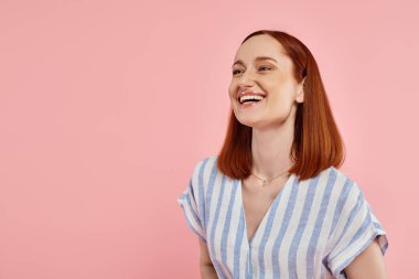 Heyecanlı, çizgili elbiseli, pembe arka planda gülen kızıl saçlı kadın. Mutluluk.