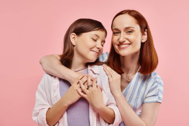 Heyecanlı ve ilham verici bir kadın pembe arka planda genç bir kızı kucaklıyor, anne ve kızın birlikteliği.