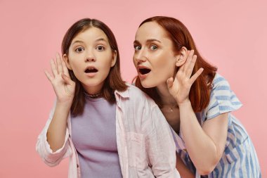 curious mother and teenage daughter holding hands near ears and eavesdropping on pink backdrop clipart