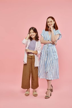 cheerful mother and preteen daughter in stylish casual clothes posing and smiling at camera on pink clipart