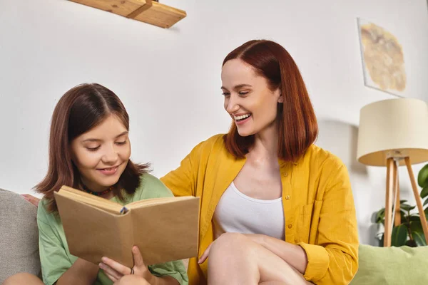 cheerful preteen girl reading special sex education literature near mother at home in living room