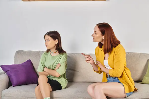serious talk, strict mother pointing at frustrated teen daughter sitting on couch in living room