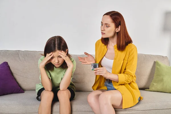 stock image mother showing condom to embarrassed teenage daughter during conversation at home, sex education