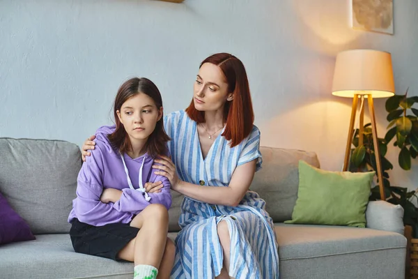 caring mother calming upset teenage daughter sitting on couch in living room, care and support