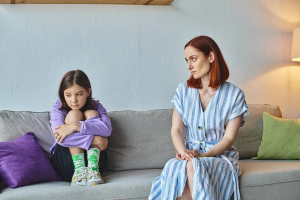 worried mother looking at depressed teenage daughter on couch in living room, supportive parent
