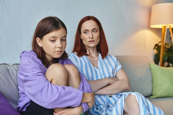 worried mother looking at depressed teenage daughter on couch in living room, supportive parent
