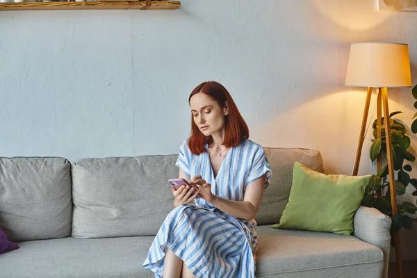 adult woman messaging on mobile phone while sitting on cozy couch in living room, domestic life