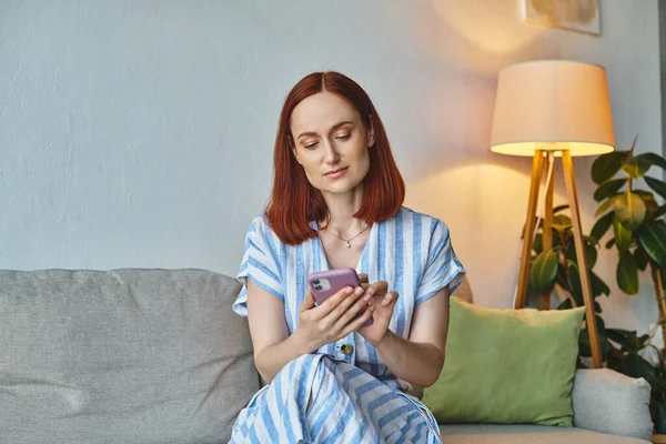 stylish woman browsing internet on smartphone on cozy couch in modern living room, domestic life