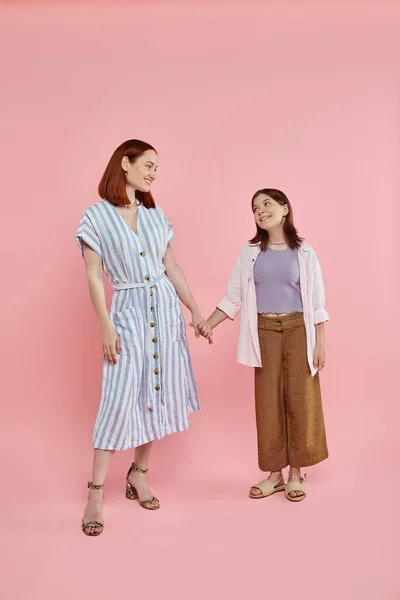 stock image full length of happy woman with teen daughter holding hands and looking at each other on pink