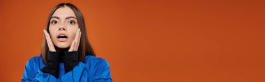 banner of shocked woman with pierced nose touching cheeks with hands and on orange backdrop clipart