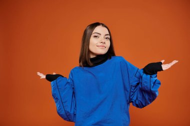 confused woman with pierced nose looking at camera while standing on orange backdrop, blue jacket clipart