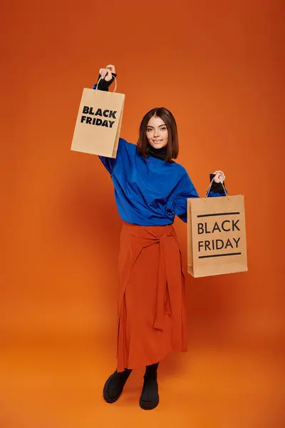 stock image full length, pretty woman in autumn outfit holding shopping bags on orange backdrop, black friday