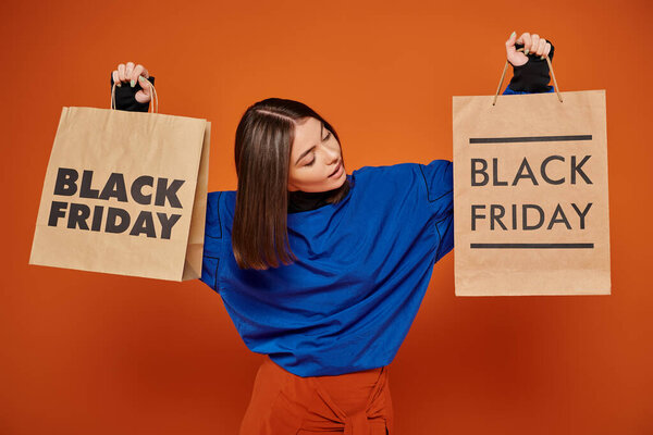 брюнетка женщина держит сумки с черными пятничными буквами на оранжевом фоне, сезон продаж