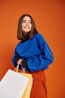 Şık sonbahar kıyafetleri içinde neşeli bir kadın siyah cuma günü alışveriş torbaları tutuyor, turuncu arka plan.