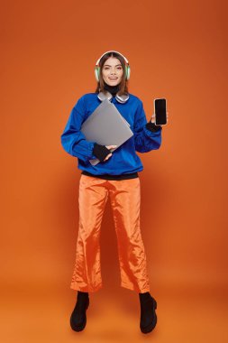 Kulaklık takan mutlu genç kadın ve sonbahar kıyafeti elinde akıllı telefon ve laptop, siber pazartesi