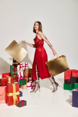 Kırmızı şenlikli elbisesi olan çekici esmer kadın yürüyor ve hediye çantaları taşıyor, bayram hediyeleri.