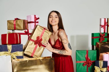 Kırmızı elbiseli mutlu çekici kadın kameraya gülümseyen hediyelerle poz veriyor, bayram hediyeleri konsepti.