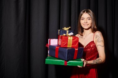 Neşeli genç bir kadın hediyeler tutuyor ve kameraya gülümsüyor perde arkası, bayram hediyeleri