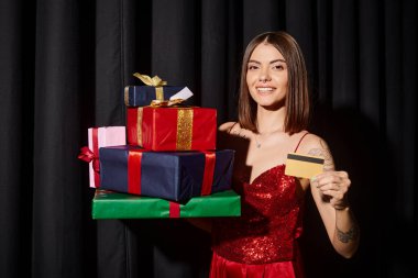 Kırmızı elbiseli çekici bir kadın hediye ve kredi kartı yığını tutuyor, bayram hediyeleri konsepti.