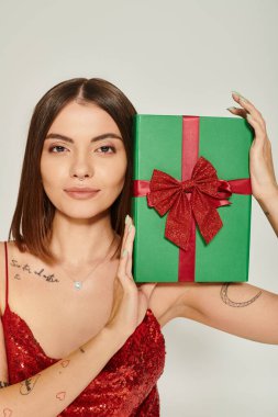 attractive woman with pierced nose and tattoos showing present at camera, holiday gifts concept clipart