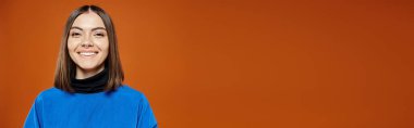 beautiful woman with pierced nose in casual blue jacket smiling at camera on orange backdrop, banner clipart