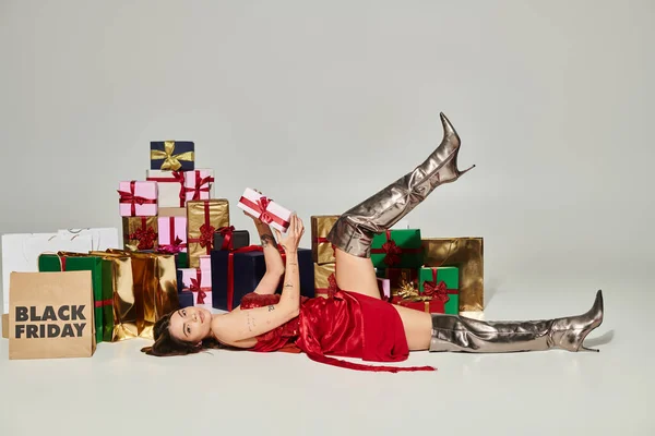 stock image attractive lady in red dress lying on floor with present in hands looking at camera, black friday