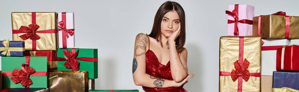 pretty lady in red attire near presents with hand on cheek looking at camera, holiday gifts, banner