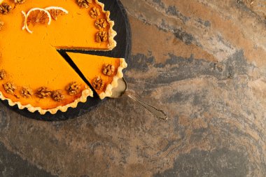 cake spatula near thanksgiving pie garnished with orange slices and walnuts on textured stone table clipart