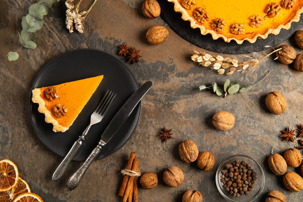thanksgiving pumpkin pie and cutlery on black plate near orange gourds on decorated stone table