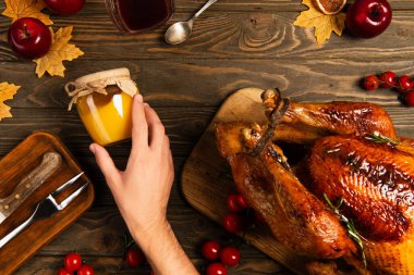 cropped view of male hand near jar of honey and thanksgiving turkey on wooden table with fall decor clipart
