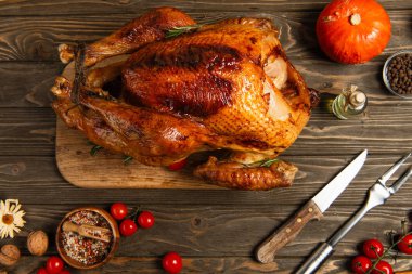 delicious thanksgiving, roasted turkey near cherry tomatoes, spices and cutlery on wooden tabletop clipart