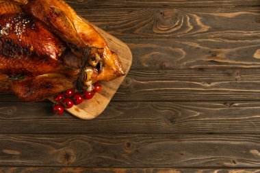 thanksgiving still life, roasted turkey on cutting board near cherry tomatoes on rustic wooden table clipart