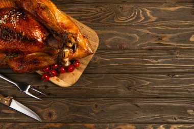 thanksgiving theme, grilled turkey on cutting board near cherry tomatoes and cutlery on wooden table clipart