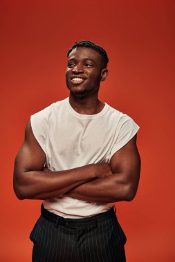 Beyaz atletli mutlu Afro-Amerikan adam kolları bağlı poz veriyor ve kırmızıya bakıyor.