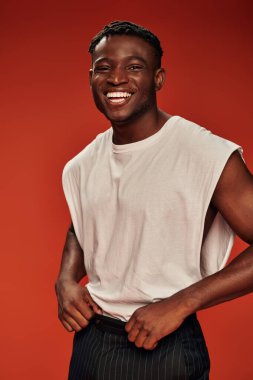 cheerful african american guy in trendy casual clothes looking at camera and laughing on red clipart