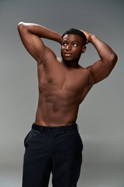 Güçlü Afro-Amerikan erkek modeli üstsüz, elleri gri üzerinde poz veriyor.