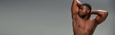 muscular and shirtless african american male model posing with hands behind head on grey, banner clipart