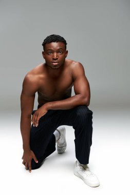athletic and shirtless african american man standing on knee and looking at camera on grey clipart