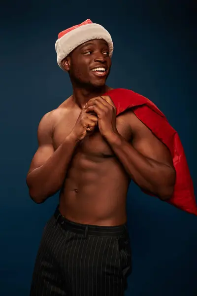 stock image cheerful african american man with shirtless torso and christmas bag looking away on navy blue
