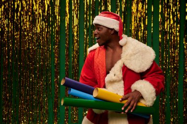 Heyecanlı Afrikalı Amerikalı Noel Baba kostümlü adam. Renkli duvar kağıtları ve parlak arkaplanı var.