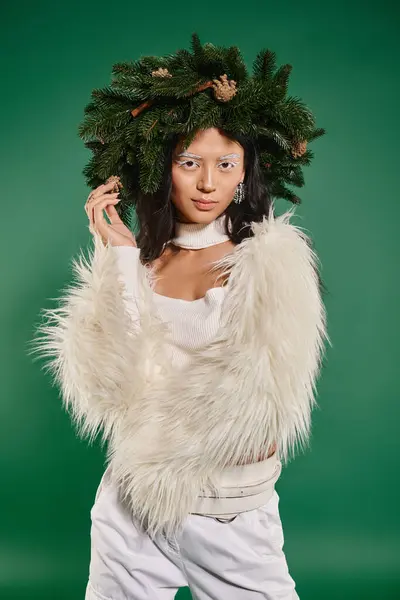 stock image winter concept, asian woman with white makeup and trendy outfit posing in wreath on green backdrop