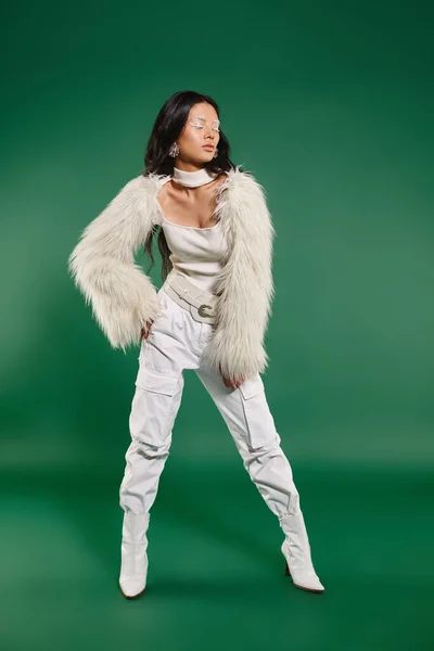 緑の背景にヒップでポーズする白い冬の服装でスタイリッシュなアジアの女性のフルサイズ — ストック写真