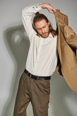 Gri arka planda bej ceket giyen beyaz gömlekli ve sakallı bir iş adamı.