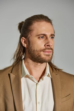 Gri arkaplanda bej ceket giyen beyaz gömlekli yakışıklı iş adamının portresi.