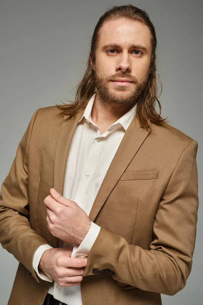 stock image handsome businessman with beard and long hair posing in blazer on grey backdrop, formal attire