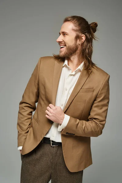 stock image cheerful businessman with beard and long hair posing in blazer on grey backdrop, formal attire