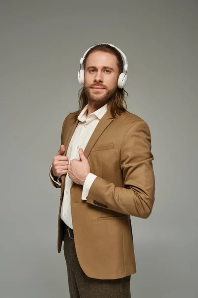 stock image cheerful bearded businessman in headphones listening music on grey backdrop, formal attire