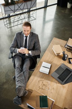 Yöneticinin rahat bir şekilde oturduğu üst görünüm ve akıllı telefonda dizüstü bilgisayar ve dizüstü bilgisayarların yanında mesajlaşması