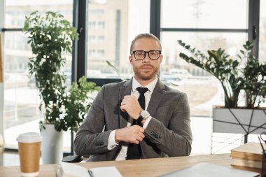 Gri takım elbiseli, gözlüklü, iş yerinde kameraya bakan kendine güvenen iş adamının portresi.